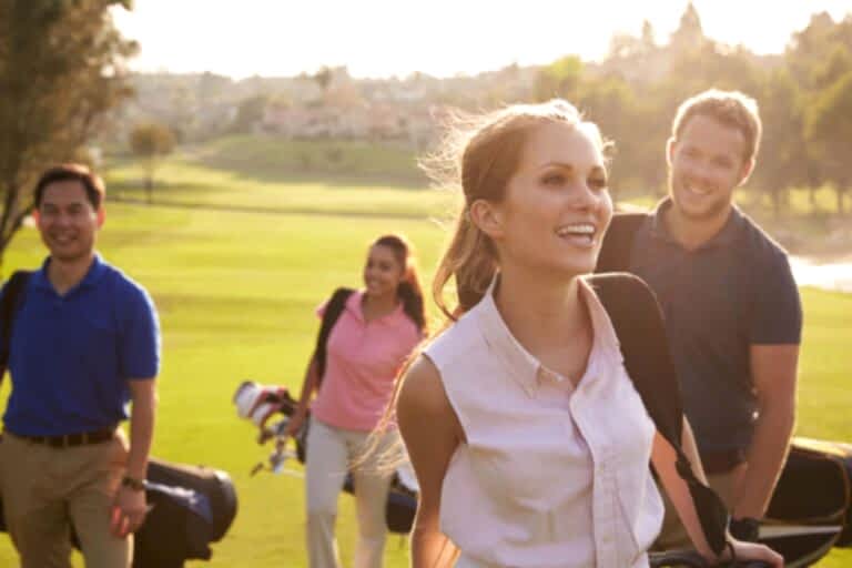 Group Of Golfers Walking Along Fairway Carrying Golf Bags