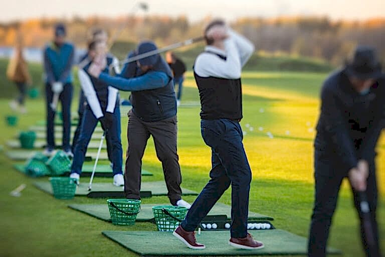 Group of golfers practicing and training golf swing on driving range practice, men playing on golf course, golf ball at golfing complex club resort, summer sunny day